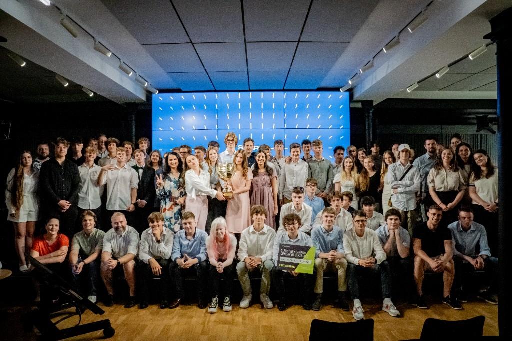 Veľká skupinová fotografia účastníkov s trofejou a oceneniami na pódiu