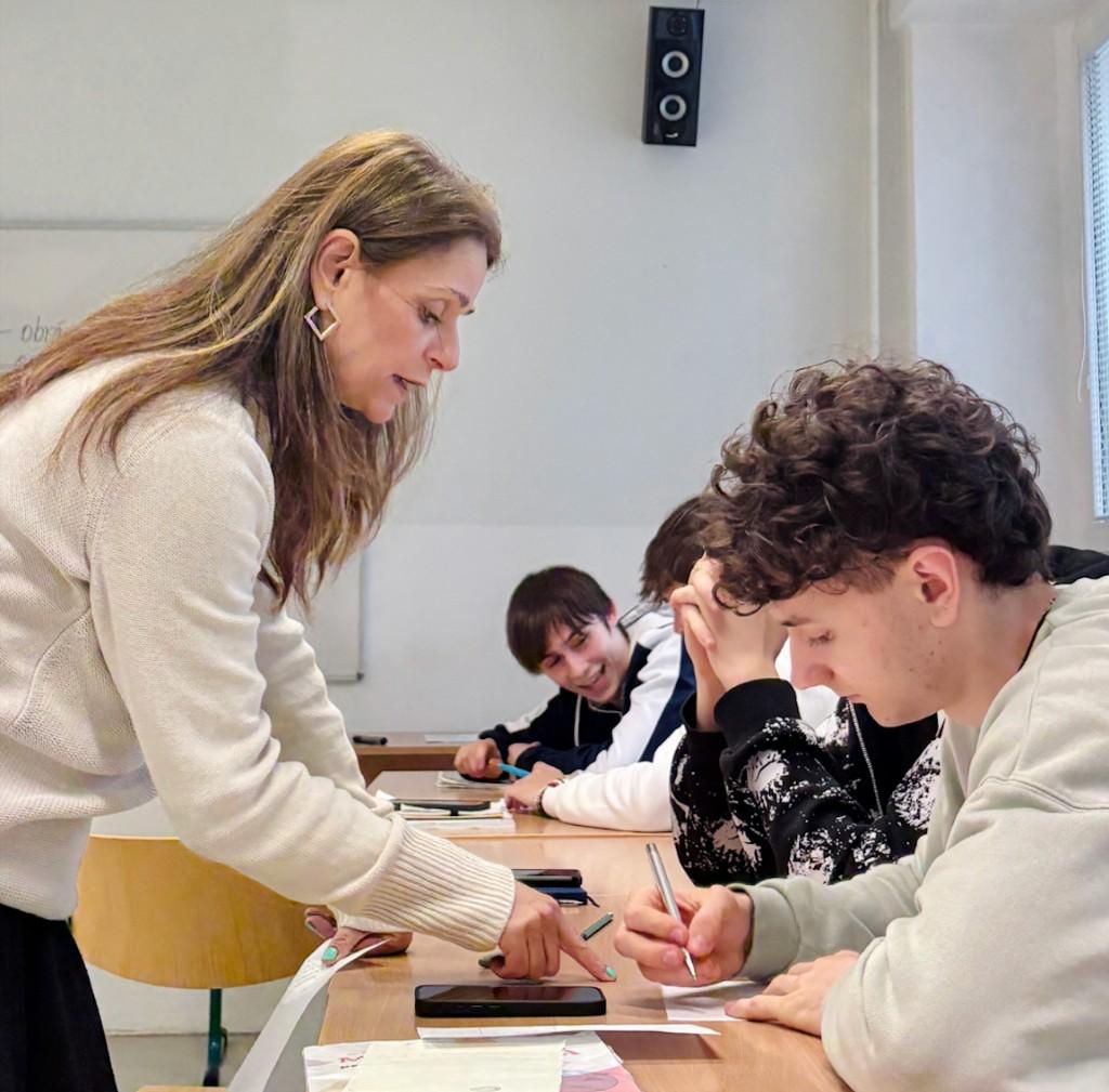 Učiteľka pri stole s študentom pri písaní v triede – podpora a sústredenie na výučbu